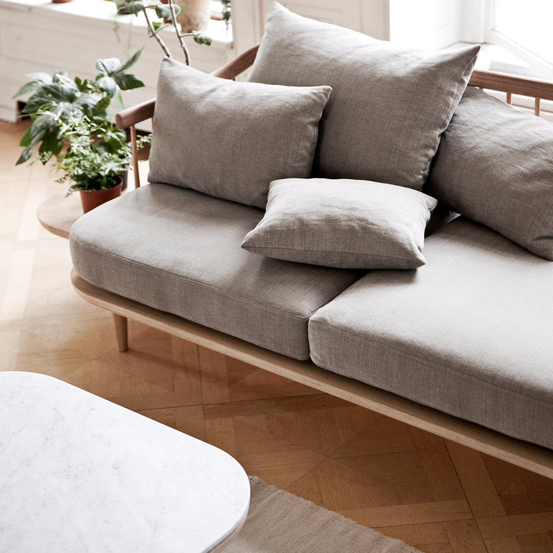 Light gray sofa with plush cushions, featuring subtle texture, complemented by wood accents and a minimalist coffee table.