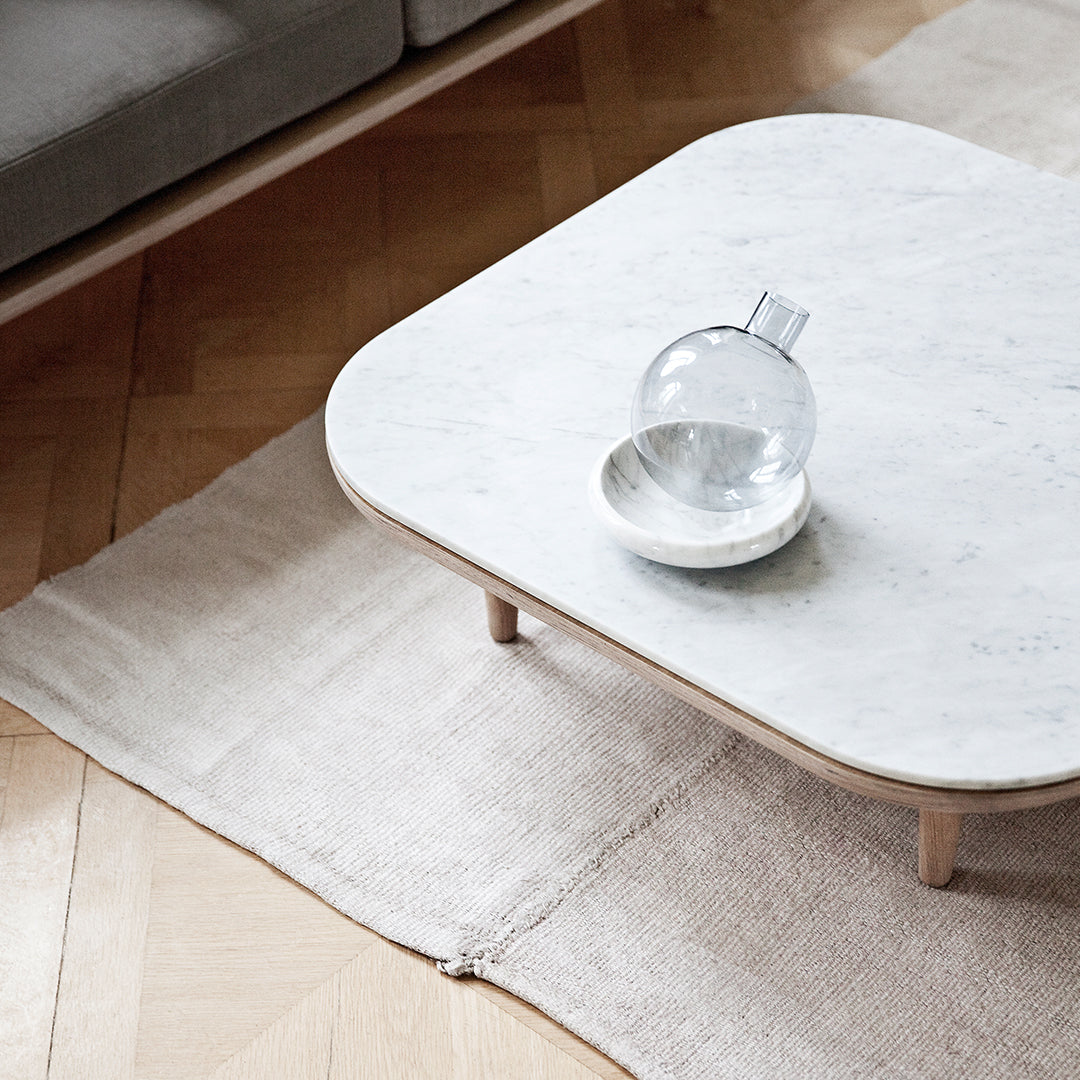 Stylish round marble coffee table with a light wood base, set on a soft beige rug, complementing modern decor.