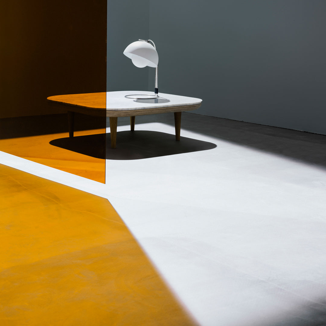 Modern coffee table on contrasting orange and white floor, with sleek lamp casting soft shadows. Minimalist design.