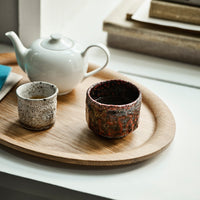 "Artisan ceramic cups in speckled white and vibrant, textured red patterns on a wooden tray."