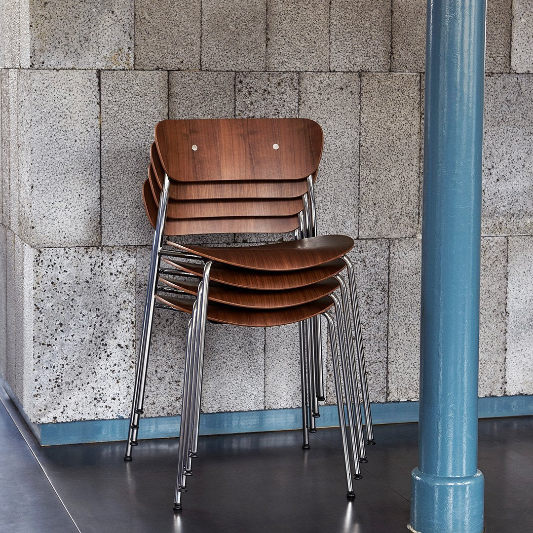 Stacked wooden chairs with a rich brown finish, featuring sleek chrome legs against a textured gray wall.