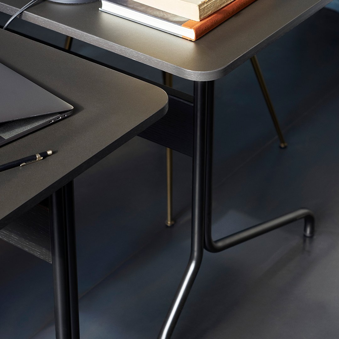 Modern black desk with sleek gray tabletop and gold accents on legs, featuring a minimalist design.