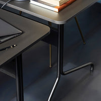 Modern black desk with sleek gray tabletop and gold accents on legs, featuring a minimalist design.