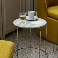 Gray marble top table with silver legs, featuring a light blue cup and yellow upholstered chair. Modern design elements.