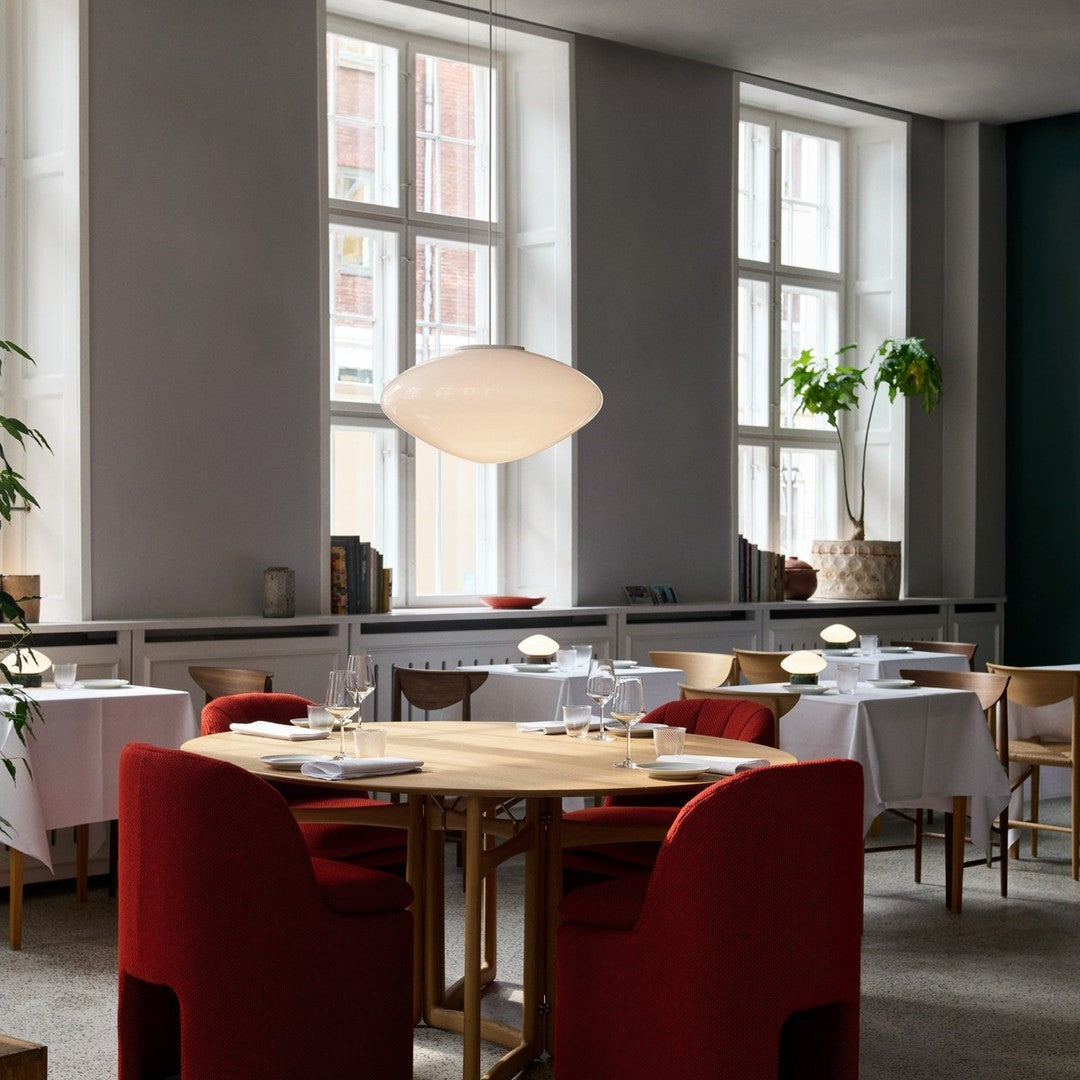 Modern dining space featuring red upholstered chairs, white table linens, and natural wood accents in a neutral-toned setting.