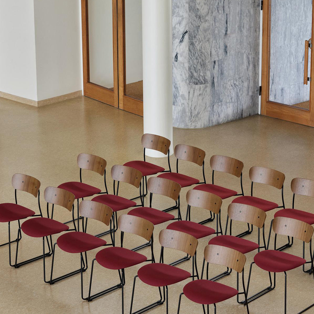 Set of minimalist chairs featuring warm wood backs and deep red upholstery against a neutral backdrop.
