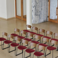Set of minimalist chairs featuring warm wood backs and deep red upholstery against a neutral backdrop.