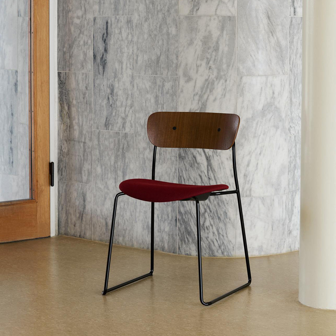 Mid-century modern chair with a dark wood backrest, vibrant red fabric seat, and sleek black metal legs against a marble backdrop.