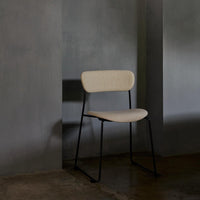 Minimalist beige chair with a sleek black metal frame against a muted gray wall. Elegant and modern design.