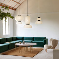 Green sectional sofa, round wooden coffee table, beige rug, and modern pendant lights in a bright, airy room.