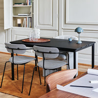 Modern black dining table with gray upholstered chairs, set against warm brown rug and soft beige walls.
