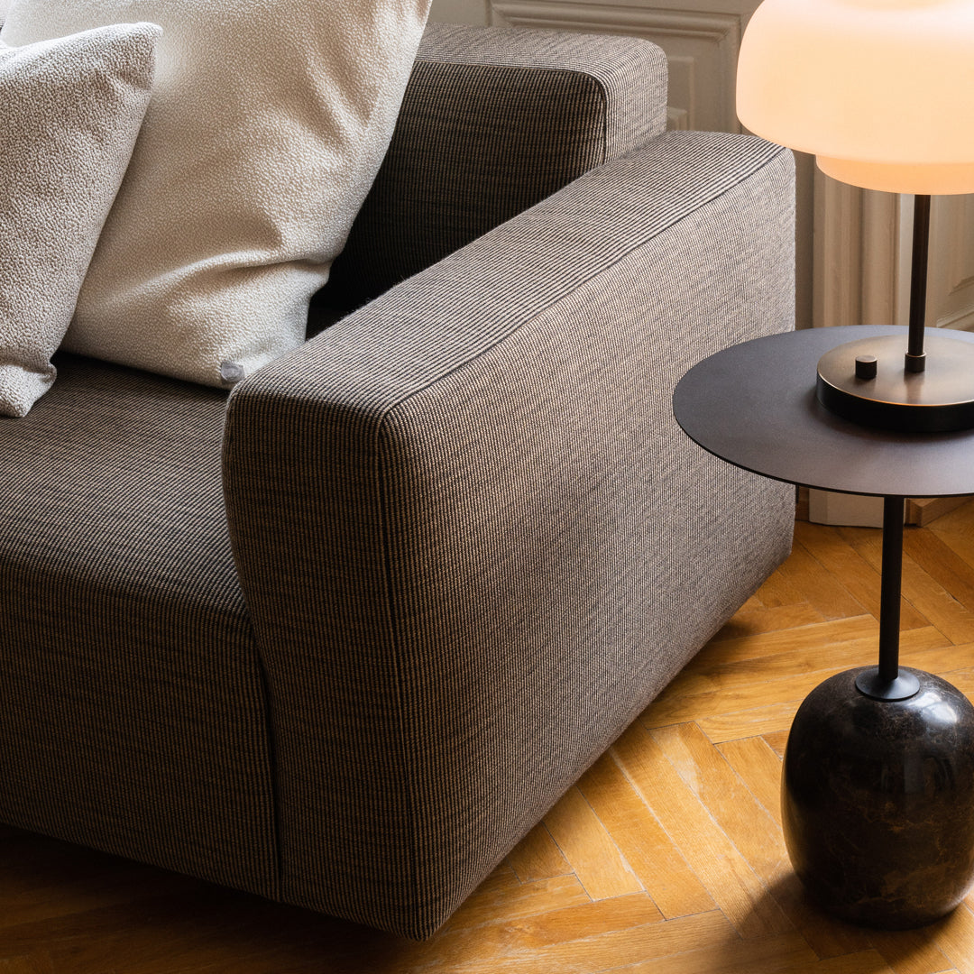 Gray textured sofa with white accent pillows, paired with a sleek black side table on a warm wooden floor.