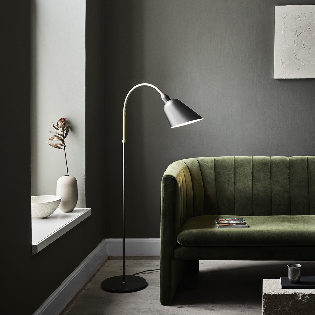 Minimalist green sofa with vertical lines, sleek black floor lamp, and neutral-toned decor against dark gray wall.