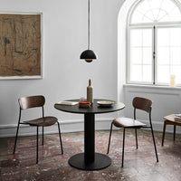 Modern dining room with a black round table, brown wooden chairs, and soft white walls featuring earthy tones.