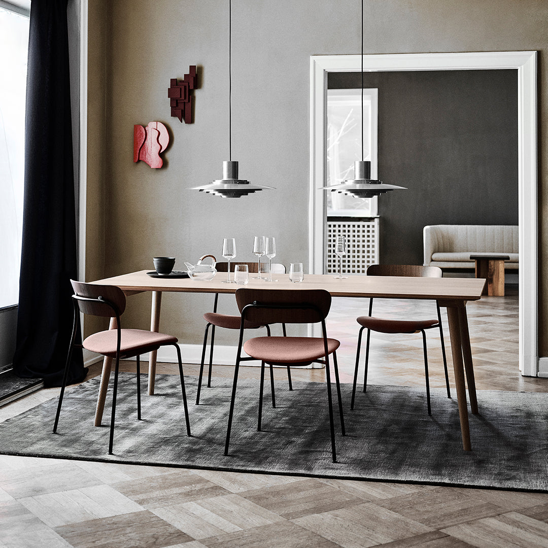 Modern dining table with light wood finish, pink chairs, gray rug, and a neutral wall with pops of red art.