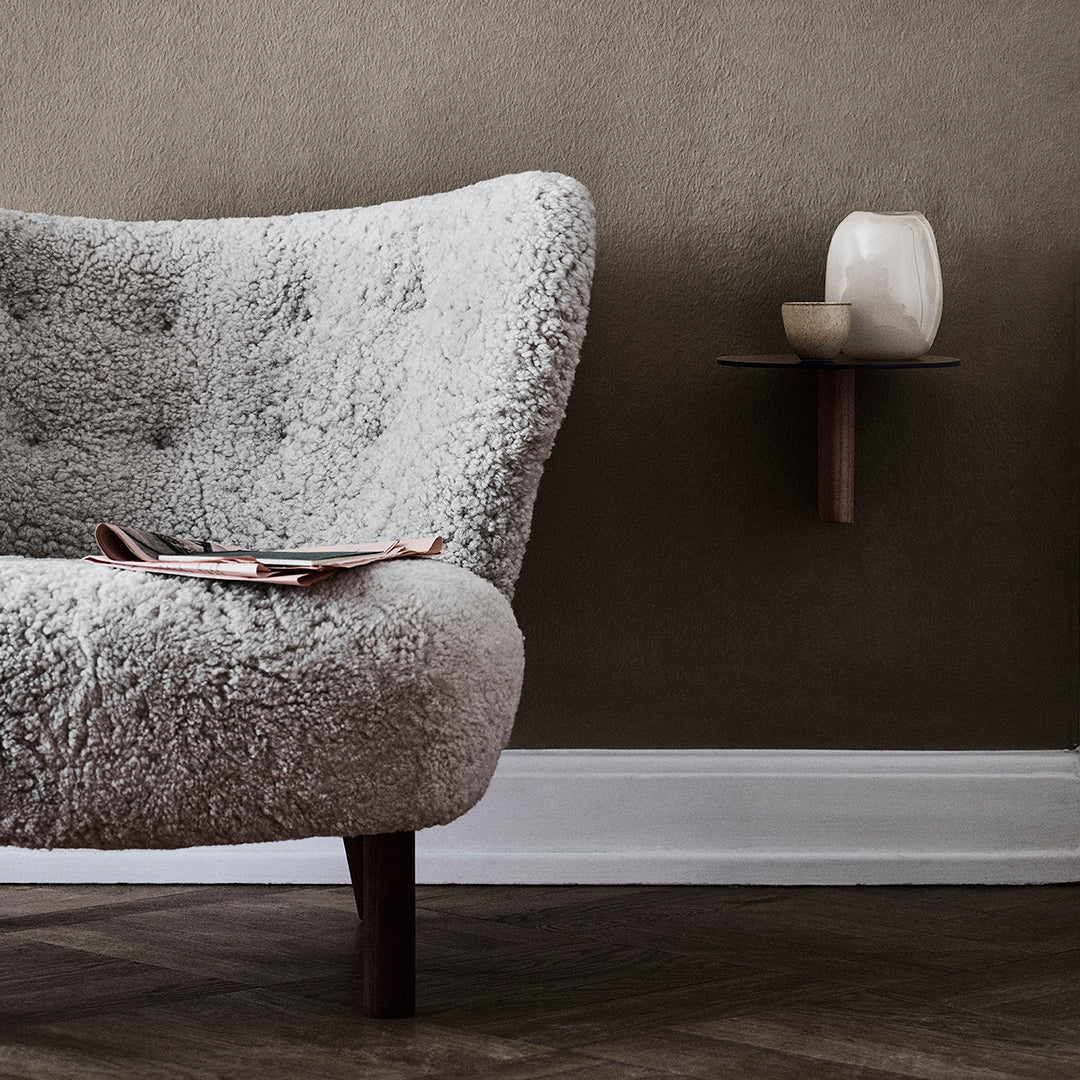 Light gray plush armchair with a textured pattern, against a warm taupe wall and brown wooden floor.