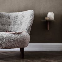 Light gray plush armchair with a textured pattern, against a warm taupe wall and brown wooden floor.