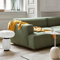 Green modern sofa with a mustard yellow throw, minimalist lamp, and neutral coffee table in a bright, airy room.