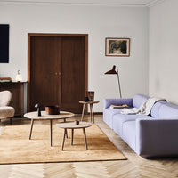 Lavender sofa, beige round rug, wooden tables, warm wood doors, minimalist design with soft neutral tones.