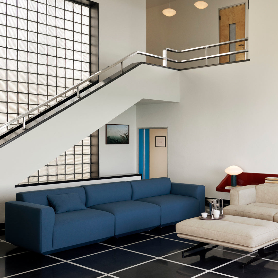 Modern blue sectional sofa on black and white checkered floor, with a minimalist beige armchair and bright wall accents.