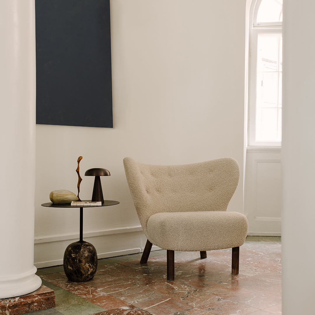 Beige tufted armchair with wooden legs against a light background, complemented by a dark blue wall and patterned floor.