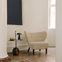 Beige tufted armchair with wooden legs against a light background, complemented by a dark blue wall and patterned floor.