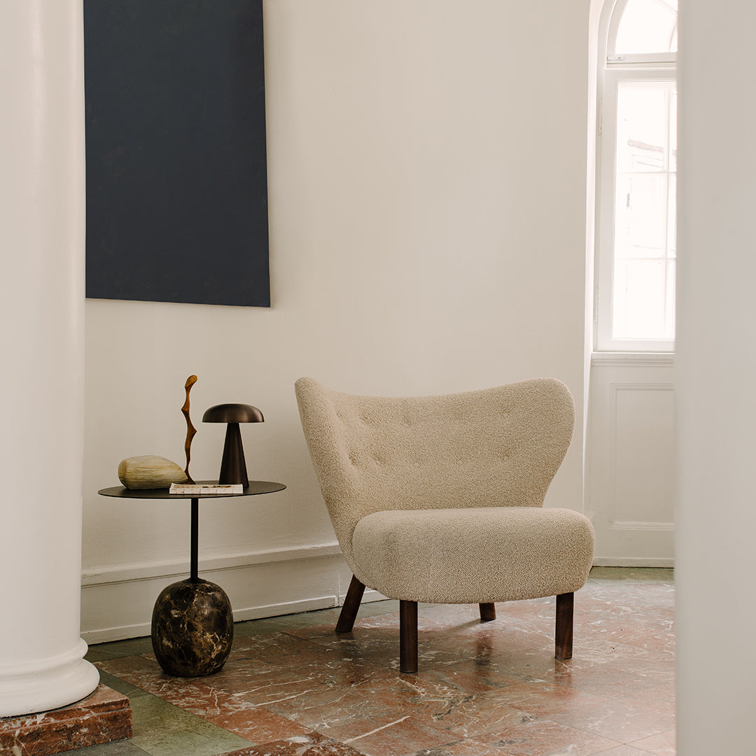 Beige tufted chair with wooden legs, set against a minimalist white wall and a dark blue abstract art piece.