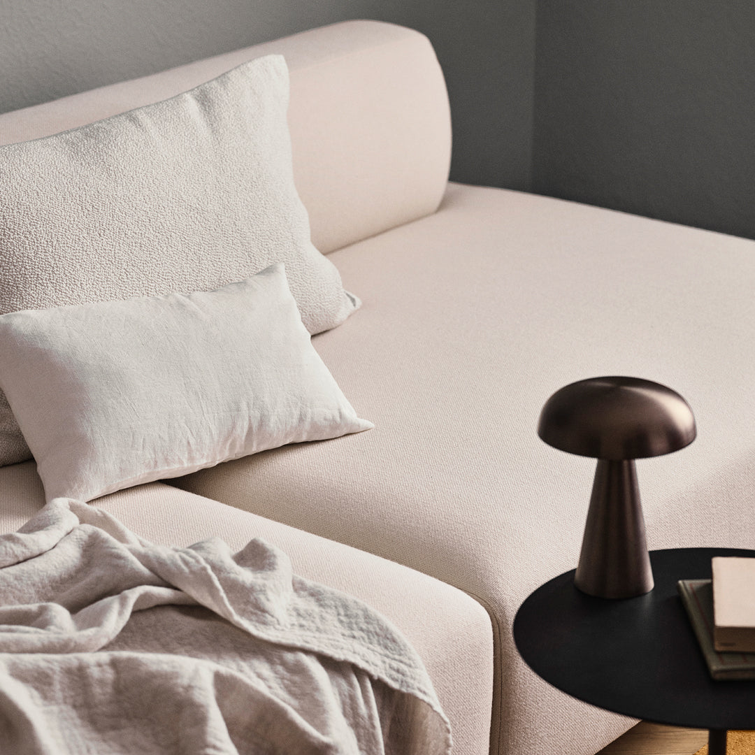 Soft pink sofa with textured white pillows, complemented by a dark bronze lamp and a light beige throw blanket.