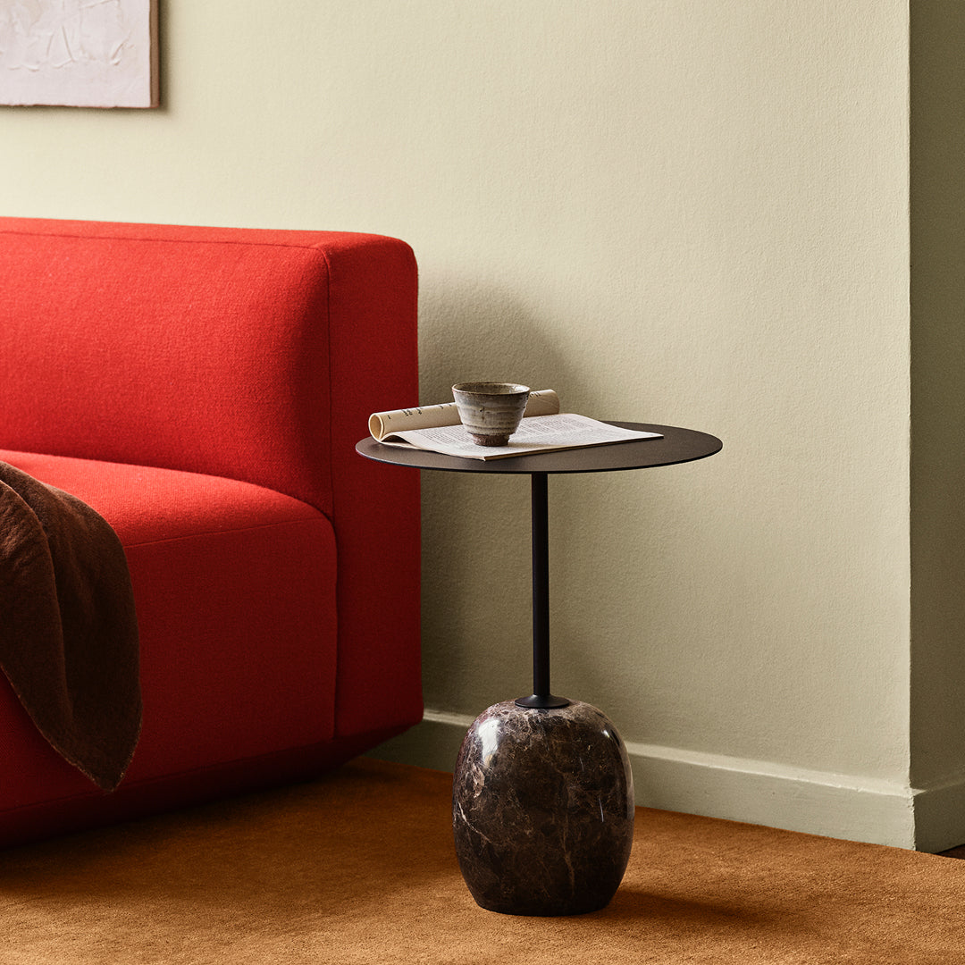 Modern black side table with a textured marble base, complementing a vibrant red sofa against a neutral backdrop.