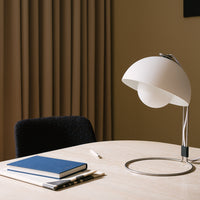 Modern white table lamp with smooth curves, paired with a navy blue notebook and dark fabric accents.