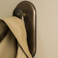 Beige coat hanging on a bronze wall hook against a textured cream background.