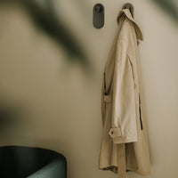 Beige trench coat hanging on a wall, complemented by a soft green accent chair and neutral background.