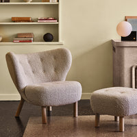 "Light beige textured chair and ottoman with natural wood legs, set against a soft green wall and minimal decor."