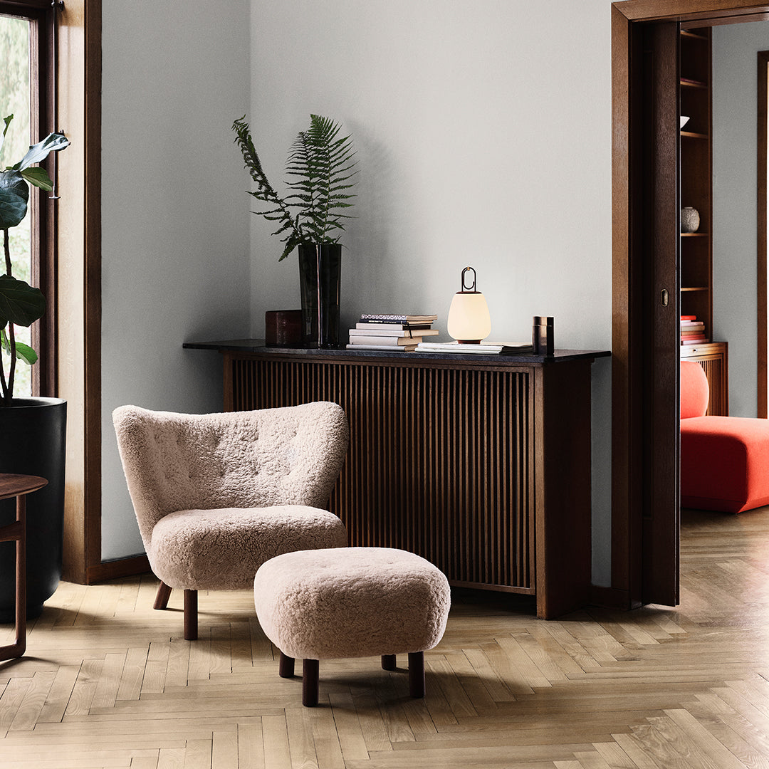 Soft beige armchair and ottoman with a textured finish, set against a neutral wall and warm wood flooring.