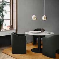 "Modern gray dining room with black circular table, dark green chairs, and warm orange rug, featuring stylish pendant lights."