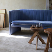 Curved blue velvet sofa with vertical stripe pattern, paired with wood accent tables on a neutral-toned floor.