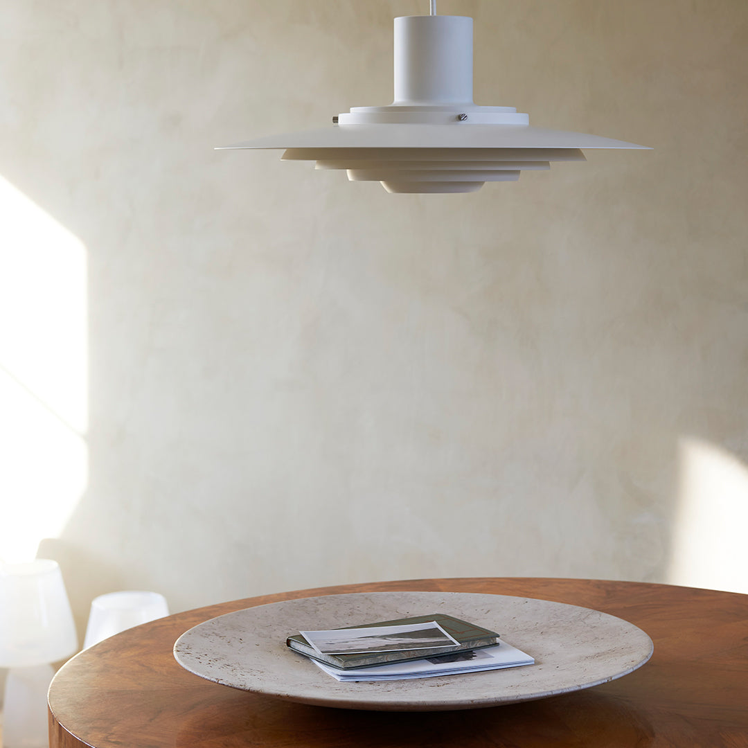 White pendant light above a round, textured beige plate on a wooden table with soft, natural lighting.