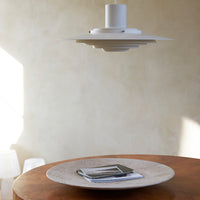 White pendant light above a round, textured beige plate on a wooden table with soft, natural lighting.