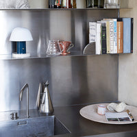 Modern kitchen shelf with metallic accents, blue and white lamp, and earthy tones in books and tableware.