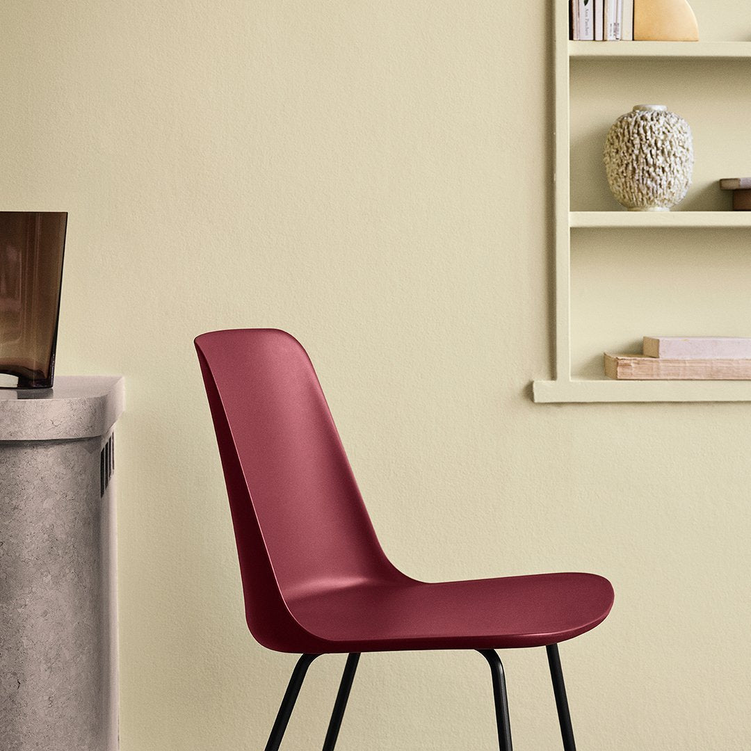 "Modern burgundy chair against a soft yellow wall, featuring sleek lines and minimalistic design."