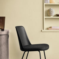 Black upholstered chair against a soft yellow wall, featuring a minimalist design and sleek lines.