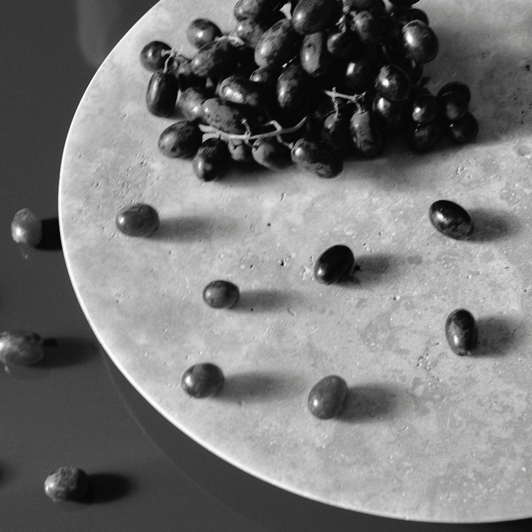 Black grapes and beans scattered on a textured gray plate, featuring a monochromatic, minimalist design.