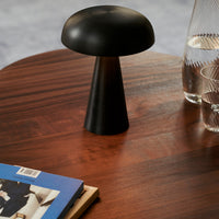 Black mushroom-shaped table lamp on a wooden surface, surrounded by modern decor and a minimalist design aesthetic.
