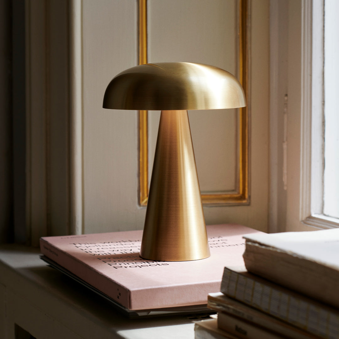 Brushed gold lamp with a sleek, minimalist design, featuring a conical base and dome shade on a soft pink book.