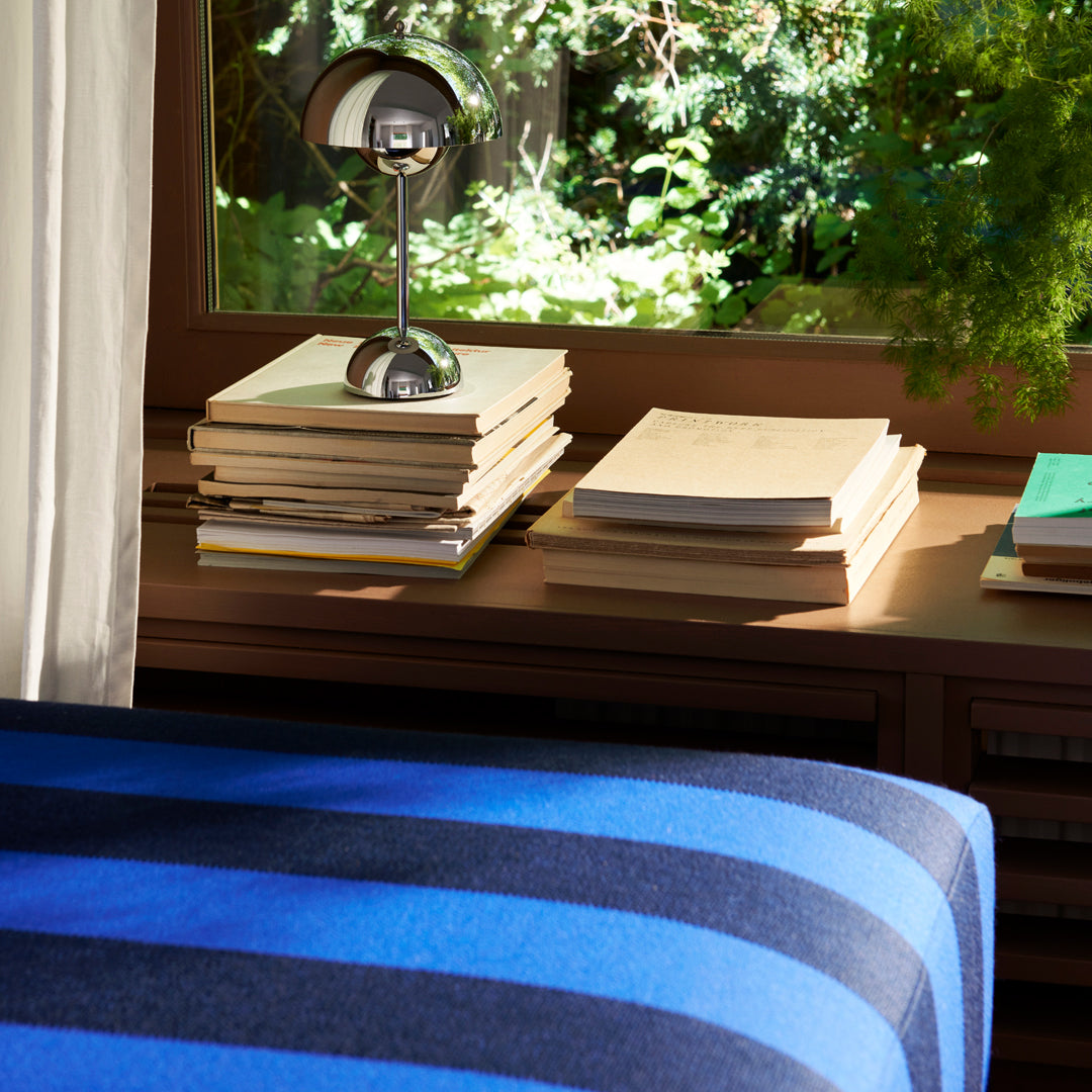 Blue striped throw blanket on a wooden table, complemented by neatly stacked books and a modern silver lamp.