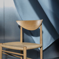 Light wood chair with a curved backrest, complemented by a soft blue backdrop and textured fabric shadows.