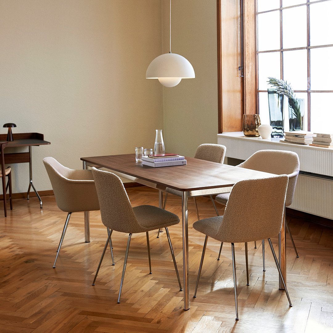 Modern wooden dining table with beige upholstered chairs against a soft, neutral backdrop and warm wooden flooring.