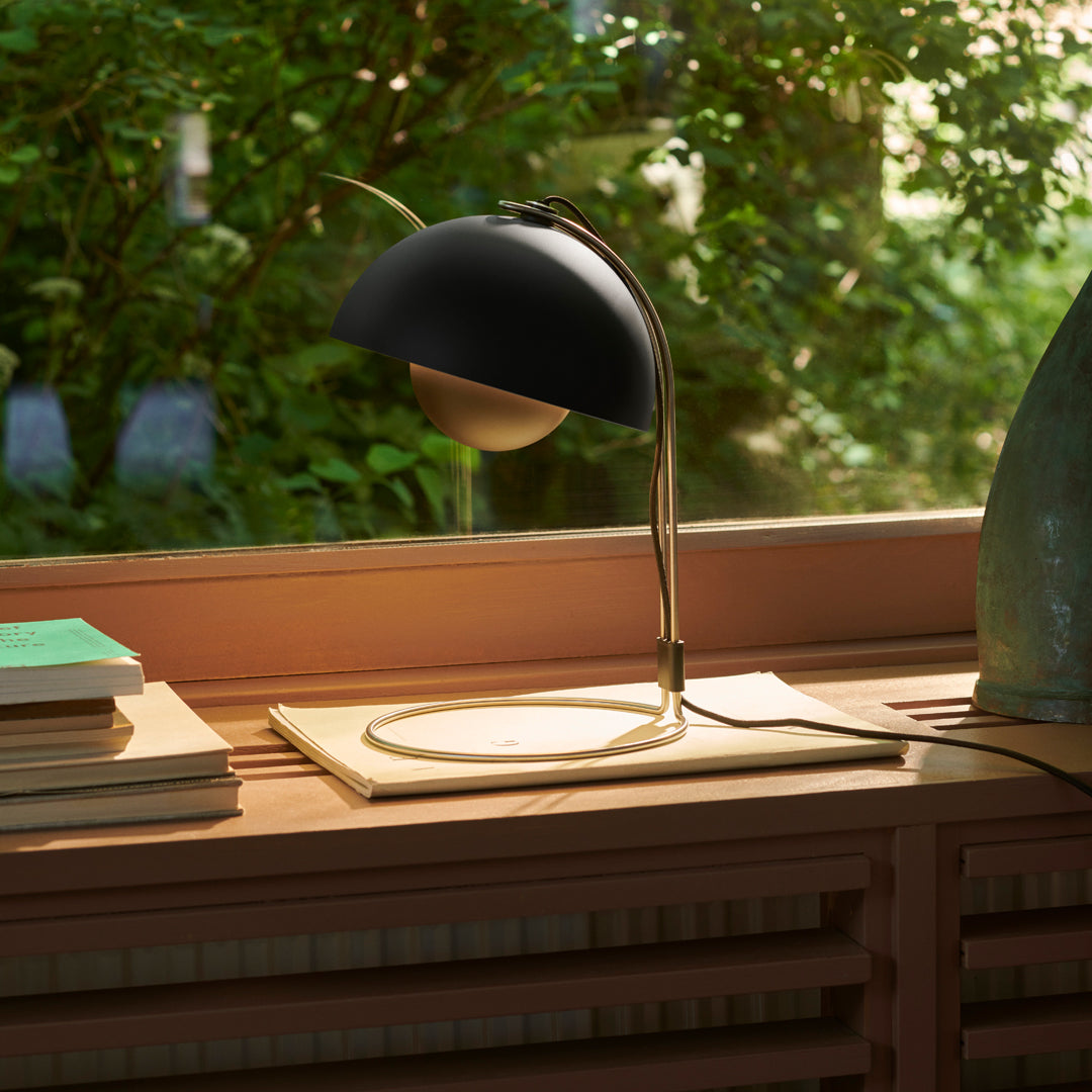 Black dome lamp with a gold interior, accompanied by stacked blue and green books, on a light wood surface.