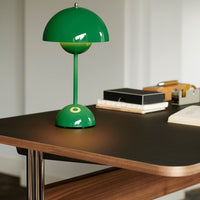 Green dome-shaped table lamp with a glossy finish, placed on a sleek wooden desk. Bright and modern design.