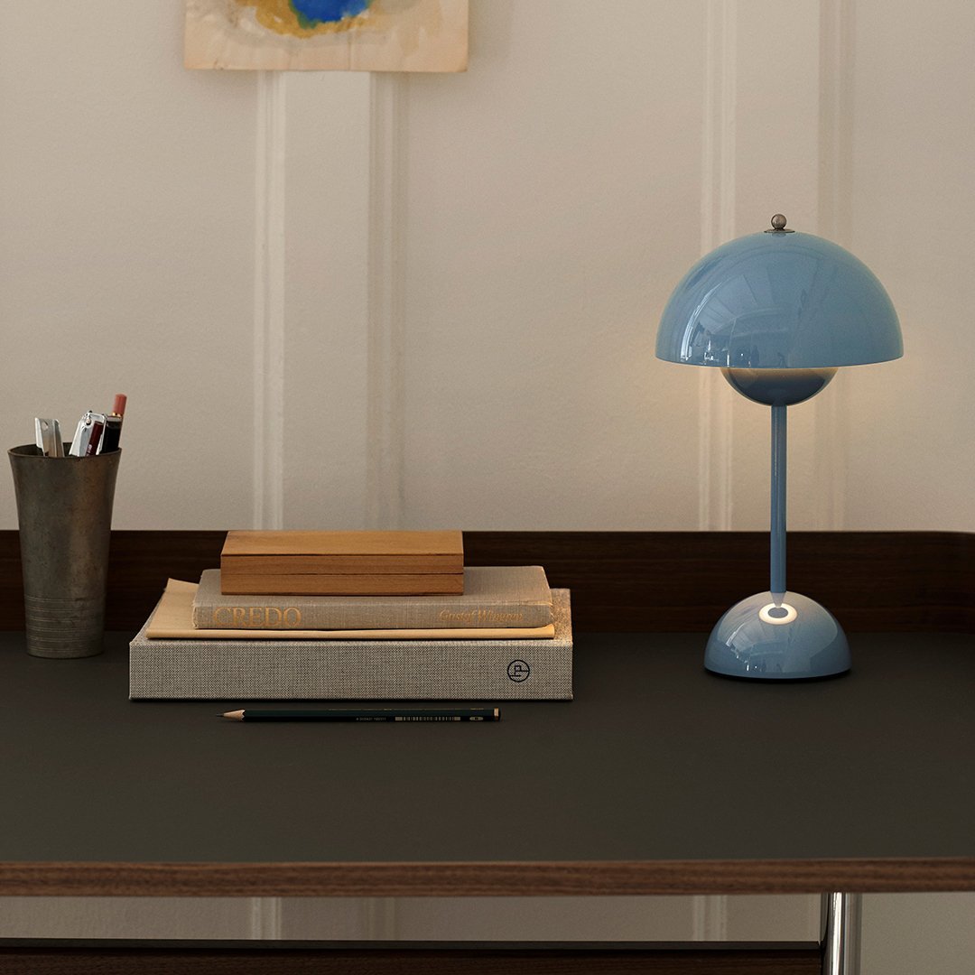 Blue lamp atop stacked books on a dark desk with subtle textures and warm lighting, enhancing a modern workspace.